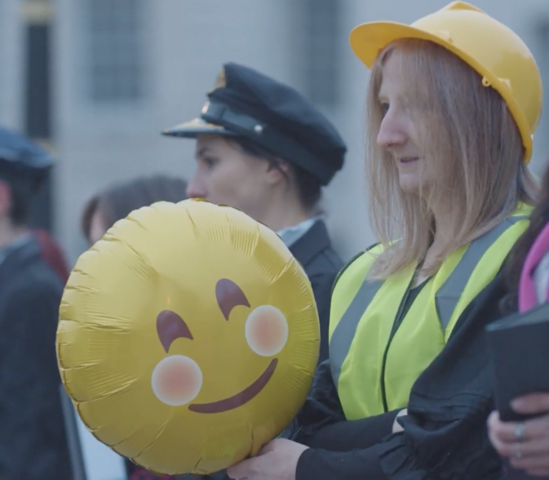 A construction worker in Trafalgar Square, London, holds a balloon with a smiley face.